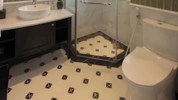 Un baño con ducha de vidrio, lavamanos blanco y retrete.
