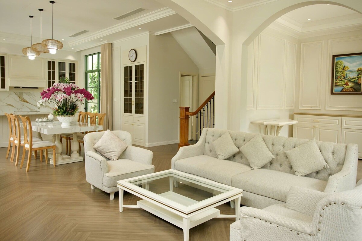 Amplia sala de estar con un sofá blanco, una mesa de centro de vidrio y una zona de comedor con mesa y sillas blancas.