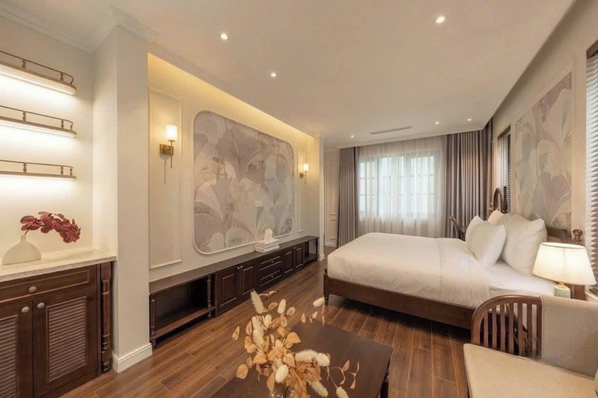 A hotel room with a large bed, a desk with a lamp, a decorative vase, and a wall-mounted artwork.