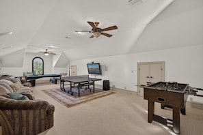 A spacious living room with a pool table, a foosball table, a sofa, and a ceiling fan. - Villa at The Cape | Concierge Services (Horseshoe Bay)