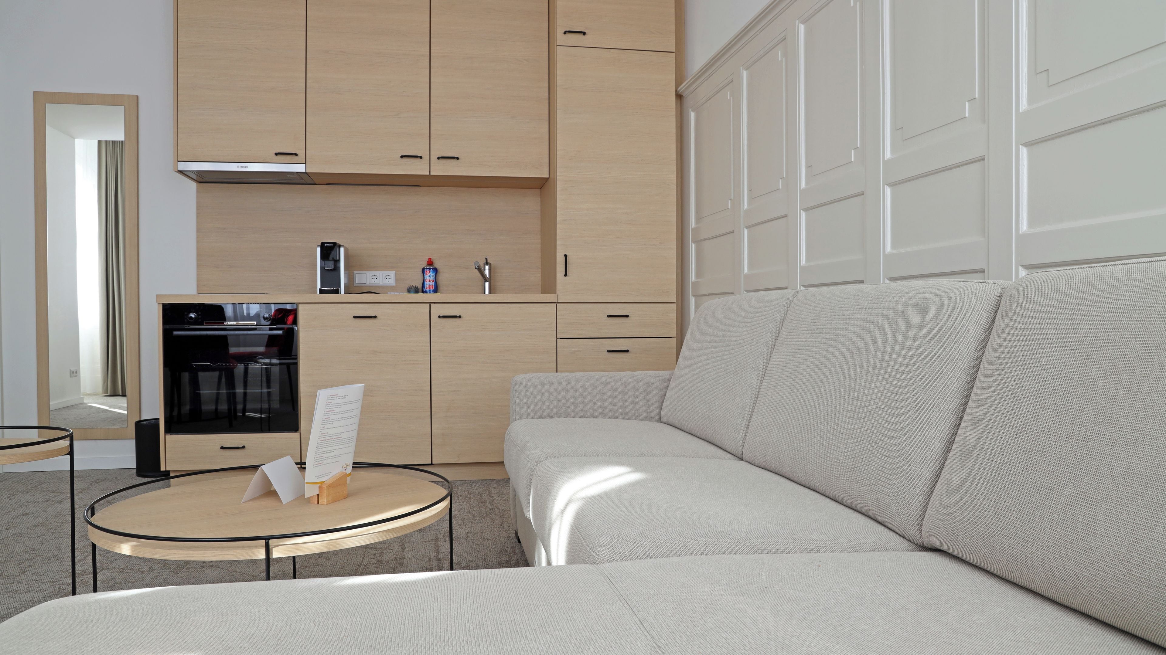 A modern living room with a sofa, a small round table, and a kitchen area with cabinets and appliances.