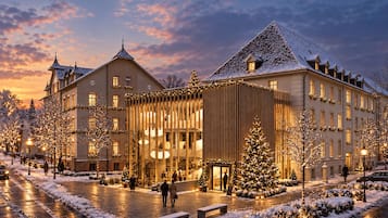 A hotel with a traditional European architectural style, featuring a prominent entrance with a glass facade and a snow-covered courtyard.