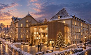 Un hotel in stile architettonico europeo tradizionale, con un ingresso ben visibile caratterizzato da una facciata in vetro e un cortile coperto di neve.