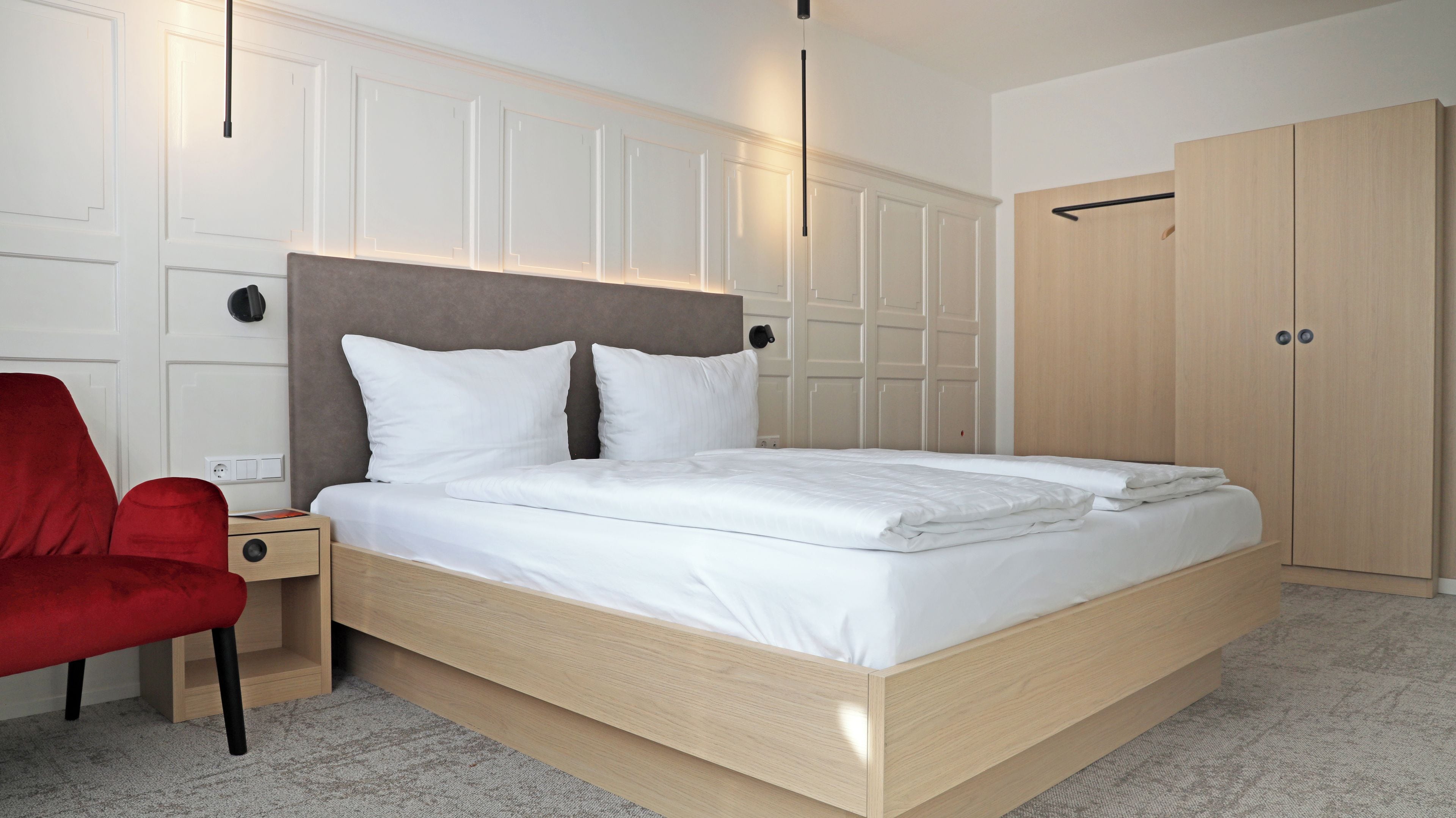 Un dormitorio moderno con una cama de madera, una silla roja, un armario y una mesita de noche.