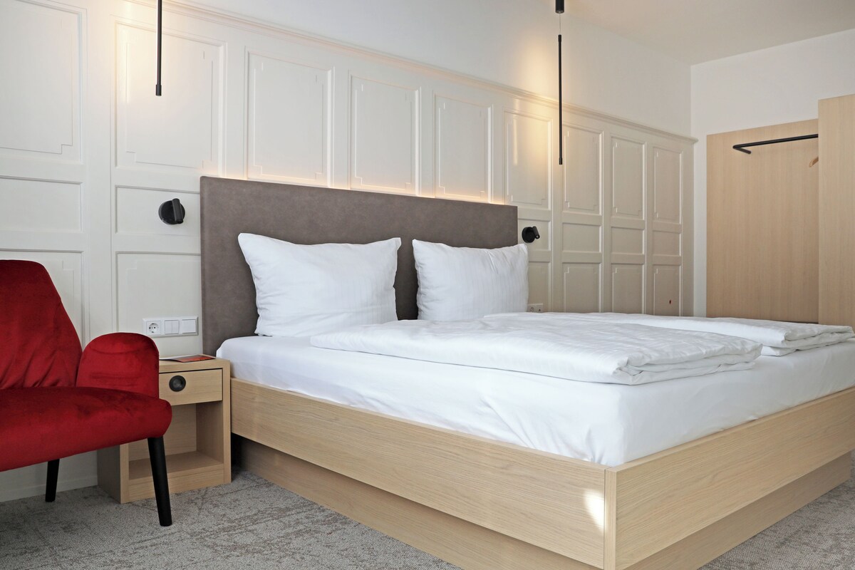 Camera da letto moderna con un letto in legno, una sedia rossa, un armadio e un comodino.