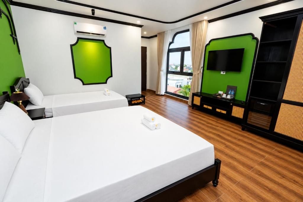 A hotel room with a large bed, a flat-screen TV, a green accent wall, and a view through a window.