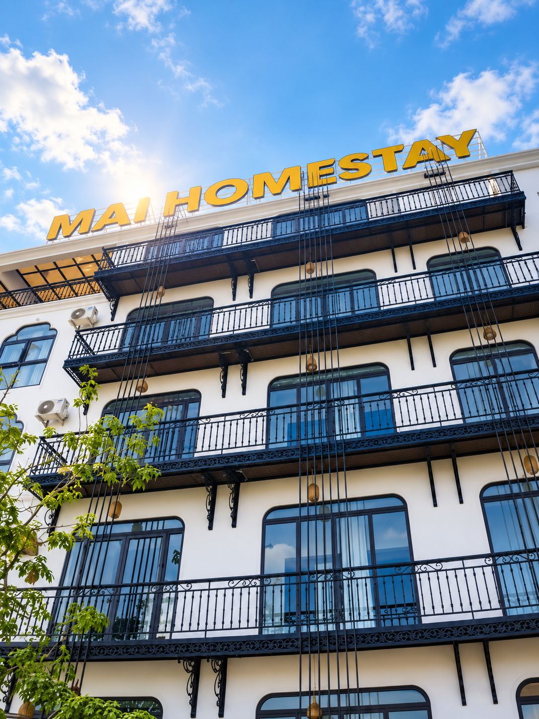 A multi-story building with balconies and a sign that reads 'MAIHOMESTAY'.