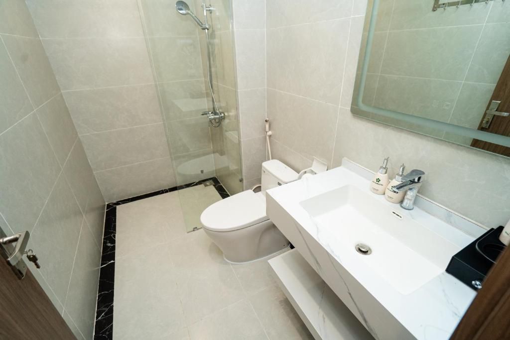 A bathroom with a glass-enclosed shower, a toilet, and a sink with a mirror above it.