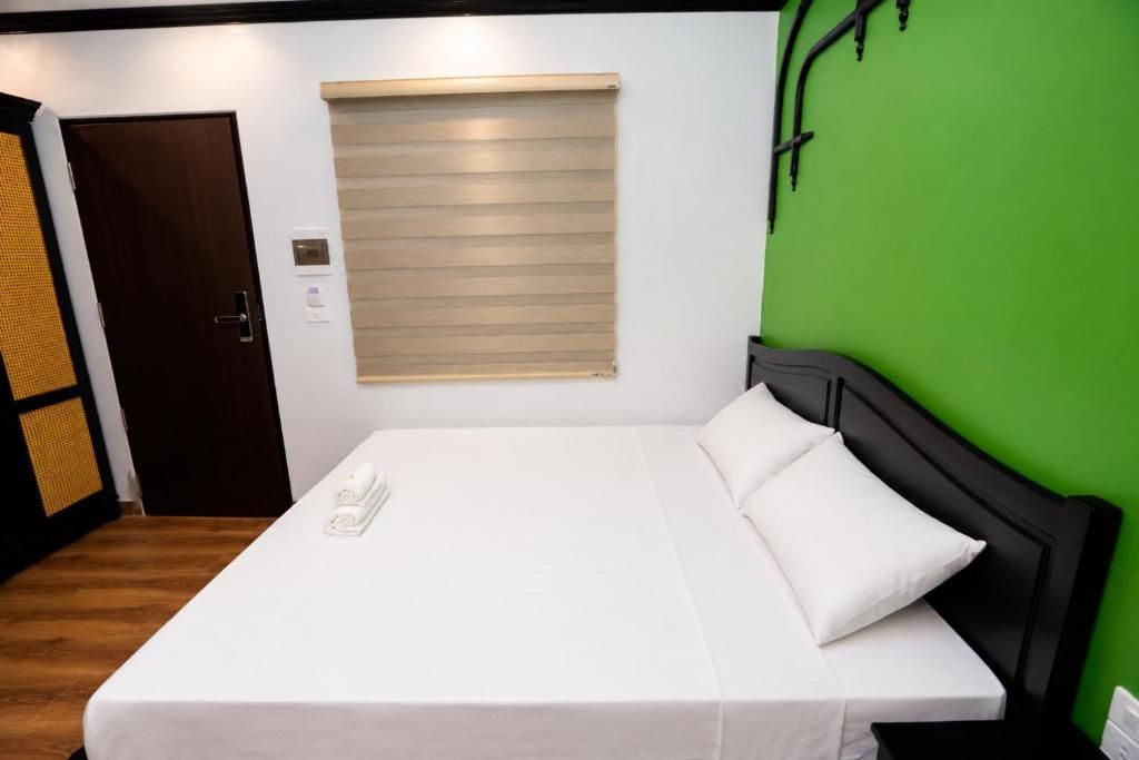 Habitación de hotel con cama, ventana con persianas, puerta y pared verde.