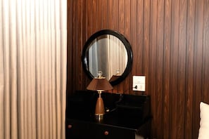 A room with a wooden panel wall, a round mirror, a black dresser with a lamp, and a white pillow. - Mai Homestay Ninh Binh (Nam Hoa Lu)