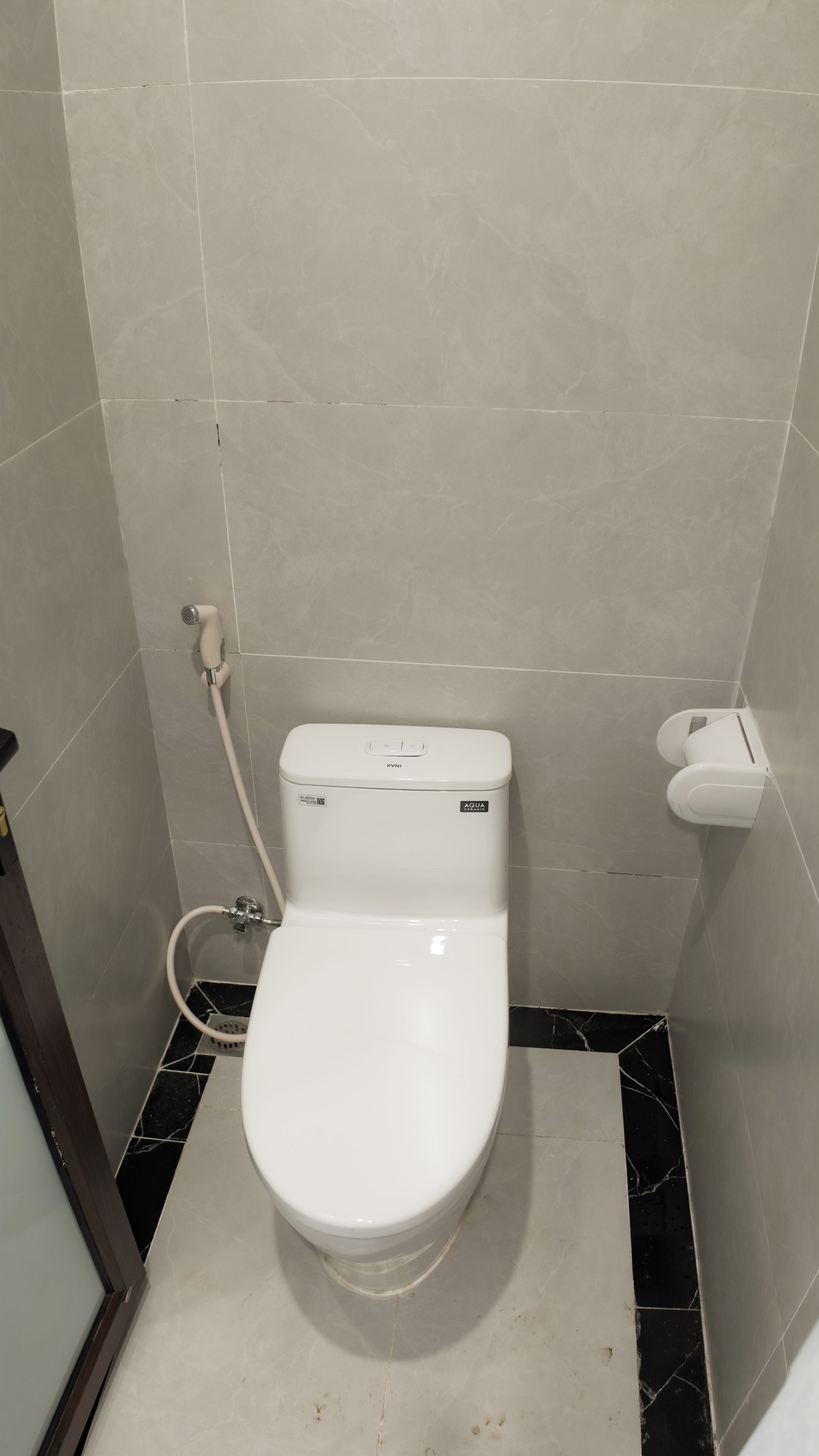 Un inodoro con panel de control, cabezal de ducha de mano y un bidet en un baño con paredes de azulejos y suelo de mármol.