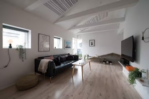 Una sala de estar moderna con un sofá de cuero negro, una mesa de centro y un televisor de pantalla plana montado en la pared.
