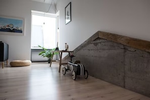Una habitación con piso de madera, una mesita con una planta, un coche de juguete y un cuadro en la pared.