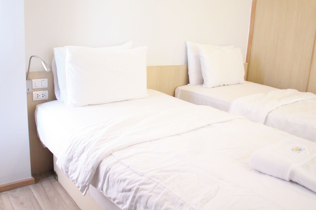 Een hotelkamer met twee bedden, elk voorzien van witte beddengoed en kussens.