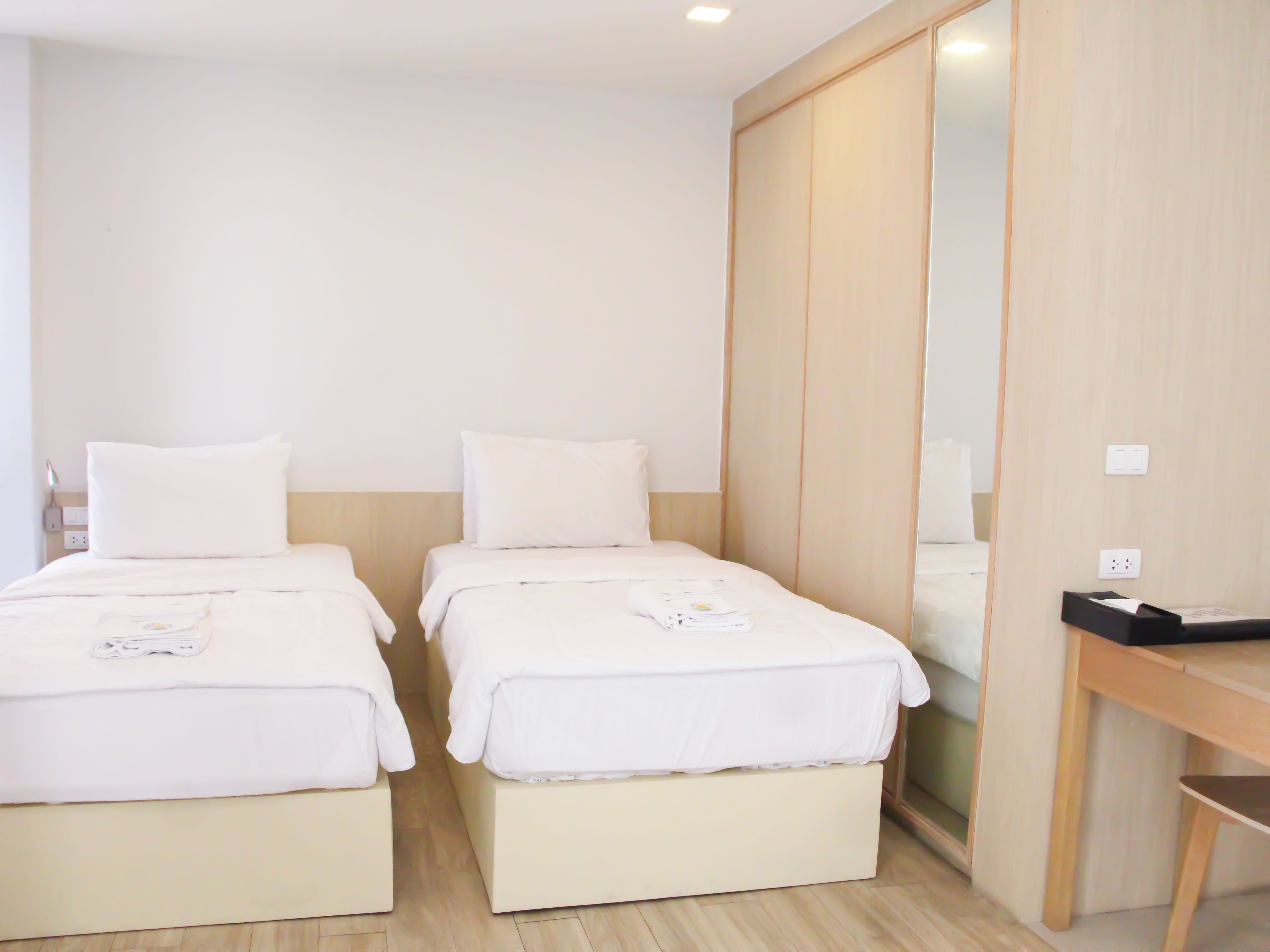 Une chambre d’hôtel avec deux lits, une armoire en bois, un bureau et un miroir.