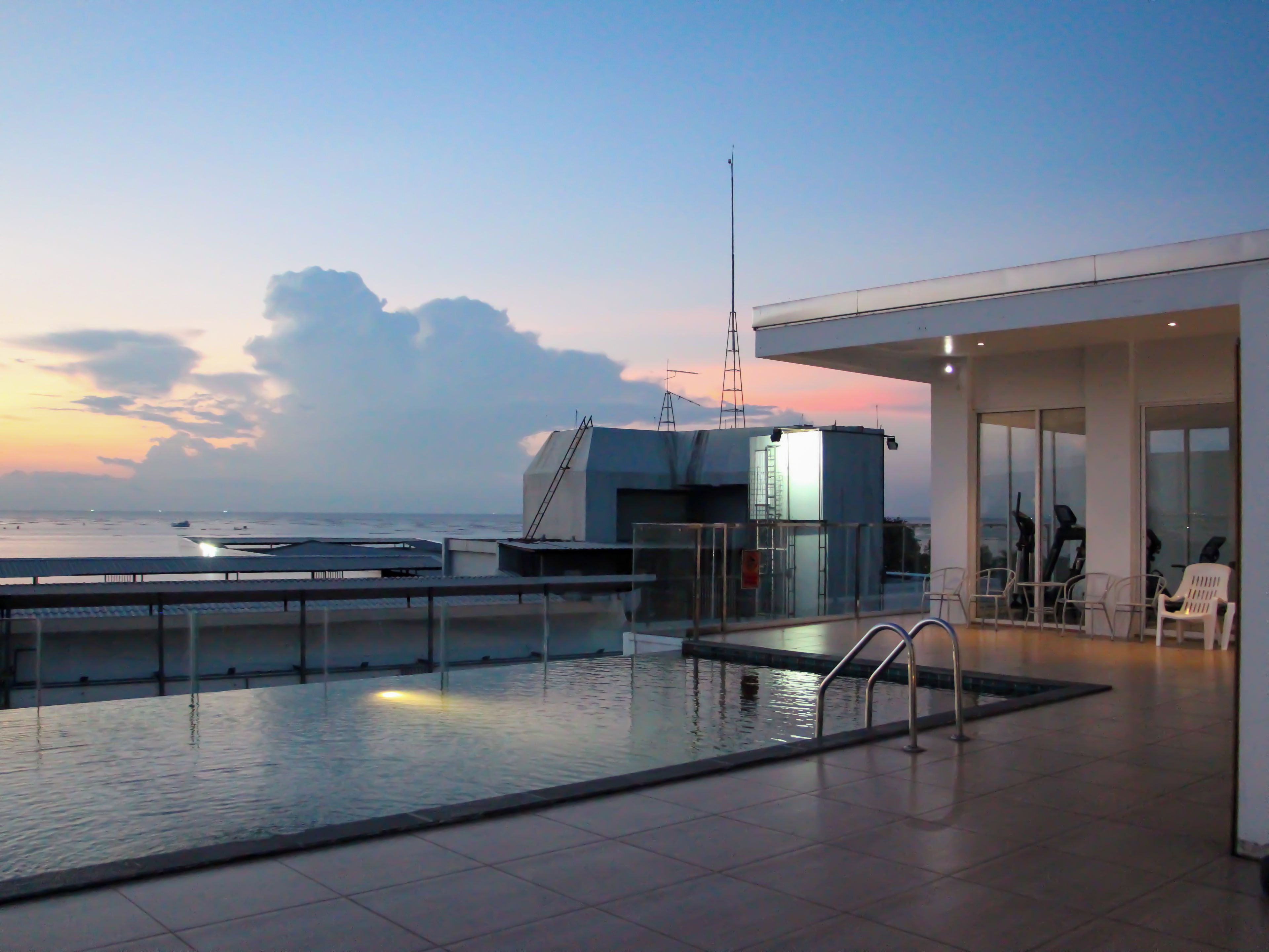 A rooftop pool with a view of the sea, a modern building with a glass facade, and outdoor seating.