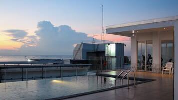 A rooftop pool with a view of the sea, a modern building with a glass facade, and outdoor seating.