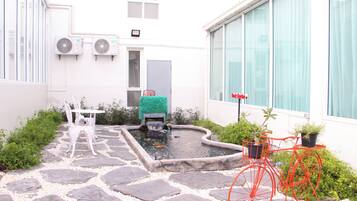 A courtyard with a stone pathway, a small pond, a red bicycle, and a white building with windows and air conditioning units.