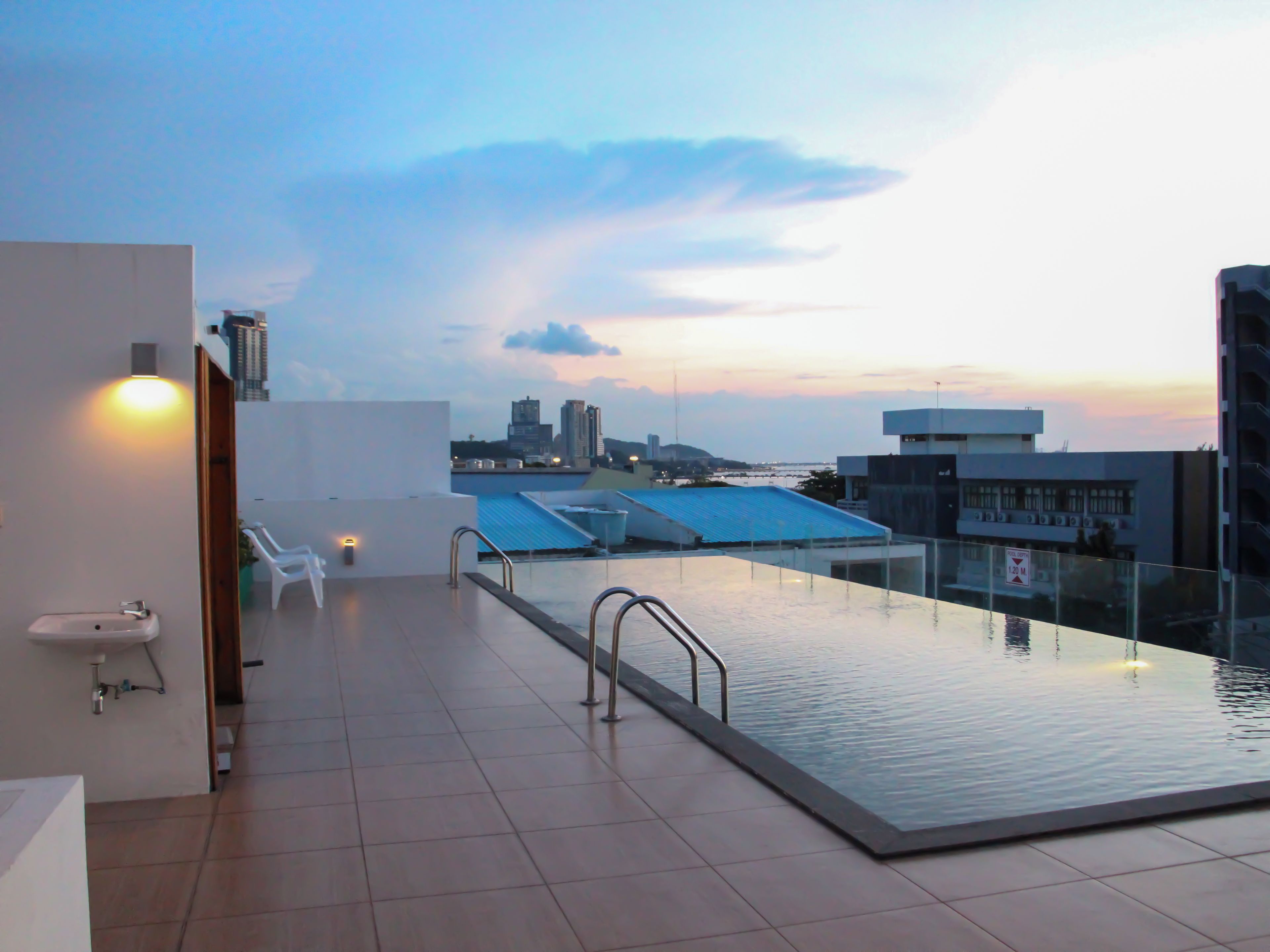 A rooftop swimming pool with a city skyline view, a white sink, and a chair.