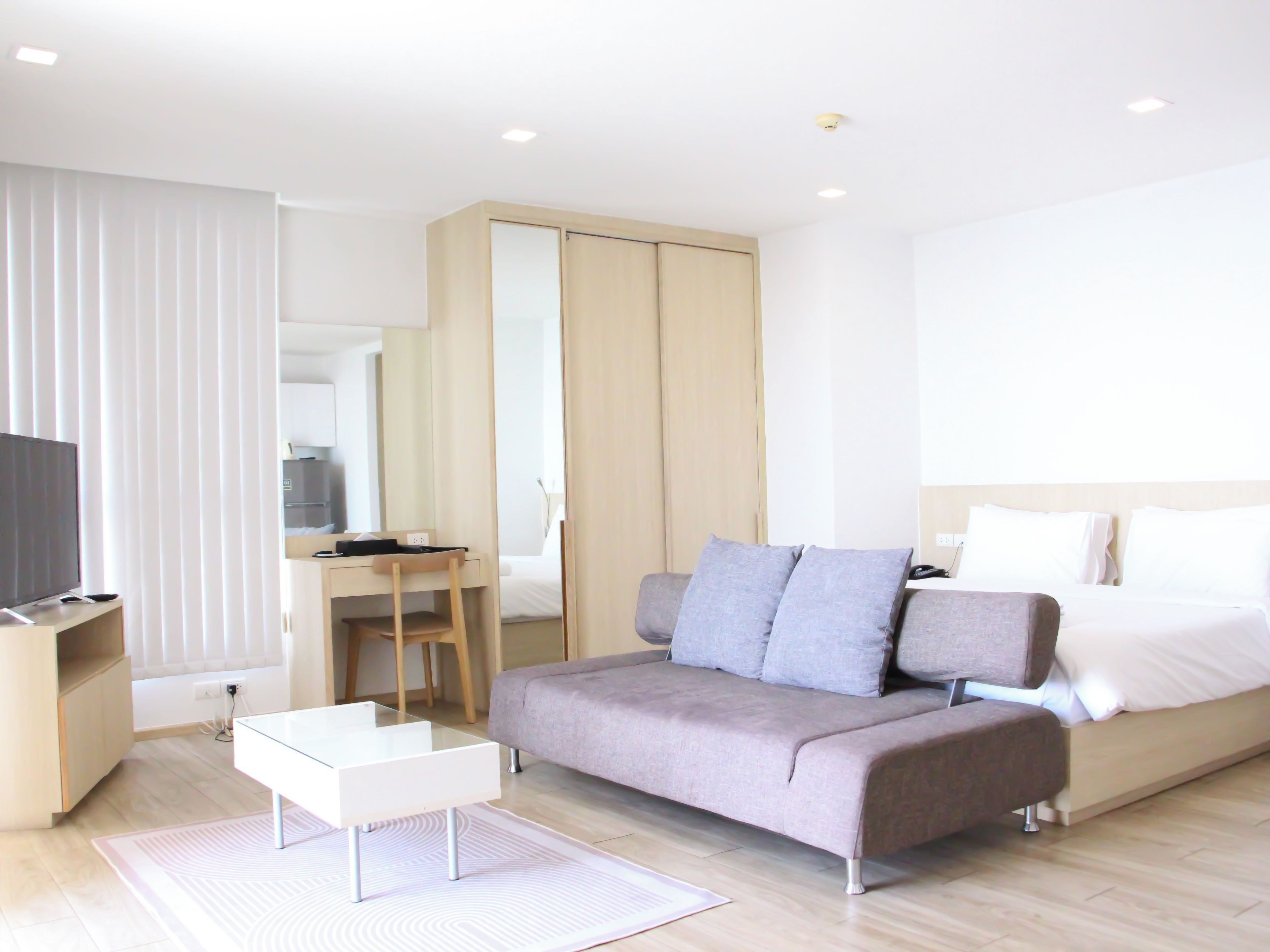 A modern hotel room with a bed, a sofa, a desk, and a television.