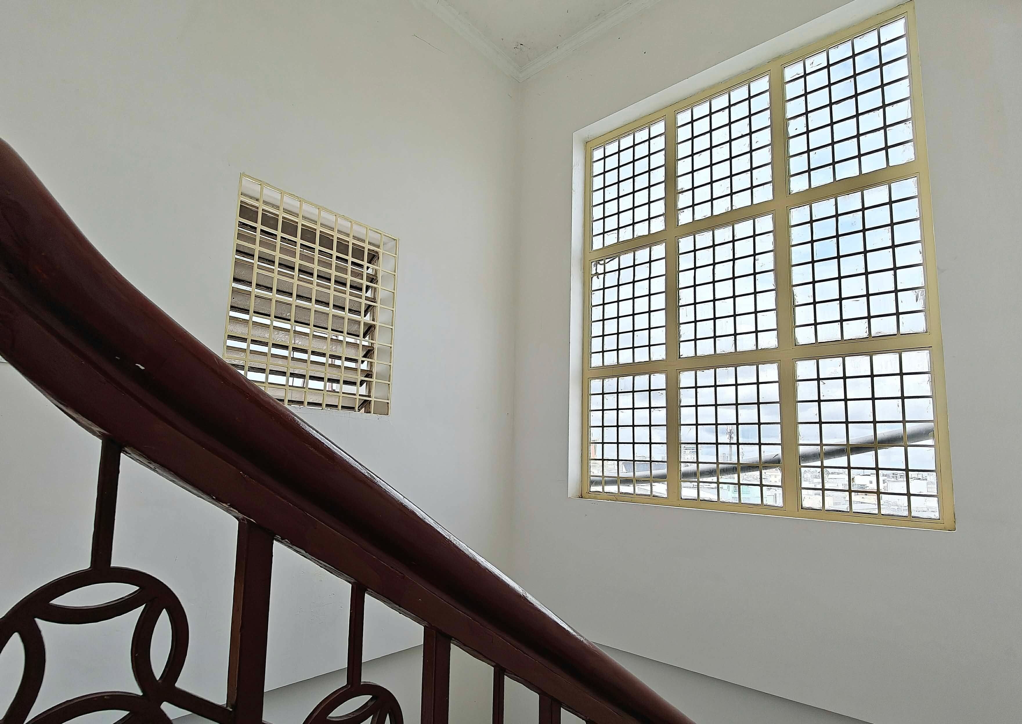 Una escalera con barandilla de madera y vista a un paisaje urbano a través de un ventanal con diseño de cuadrícula.