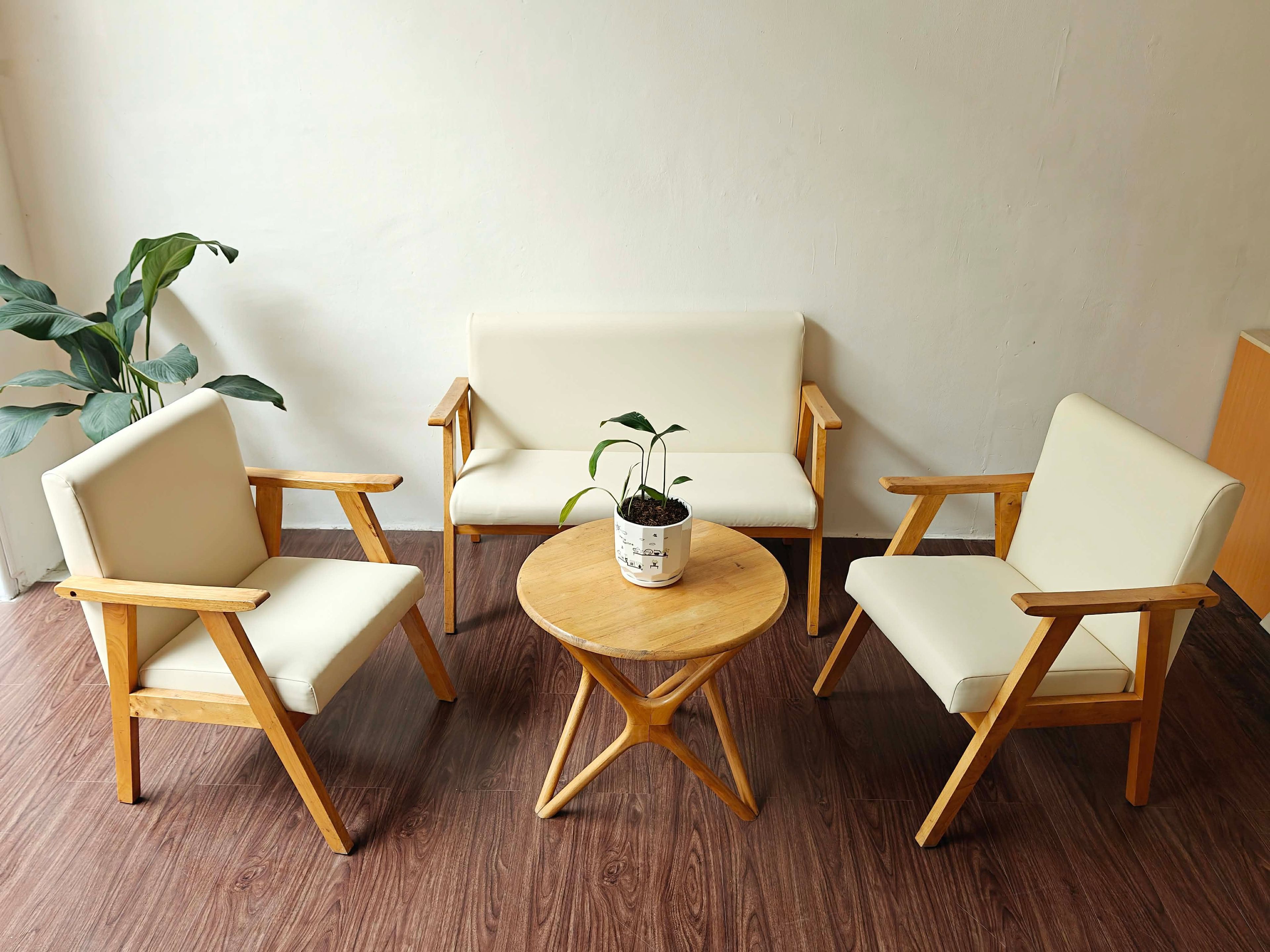 Una habitación con una mesa redonda de madera, dos sillas blancas con cojines y una planta en maceta.