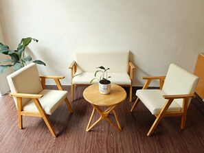 A room with a round wooden table, two white cushioned chairs, and a potted plant. - J Guesthouse (Ninh Kieu)