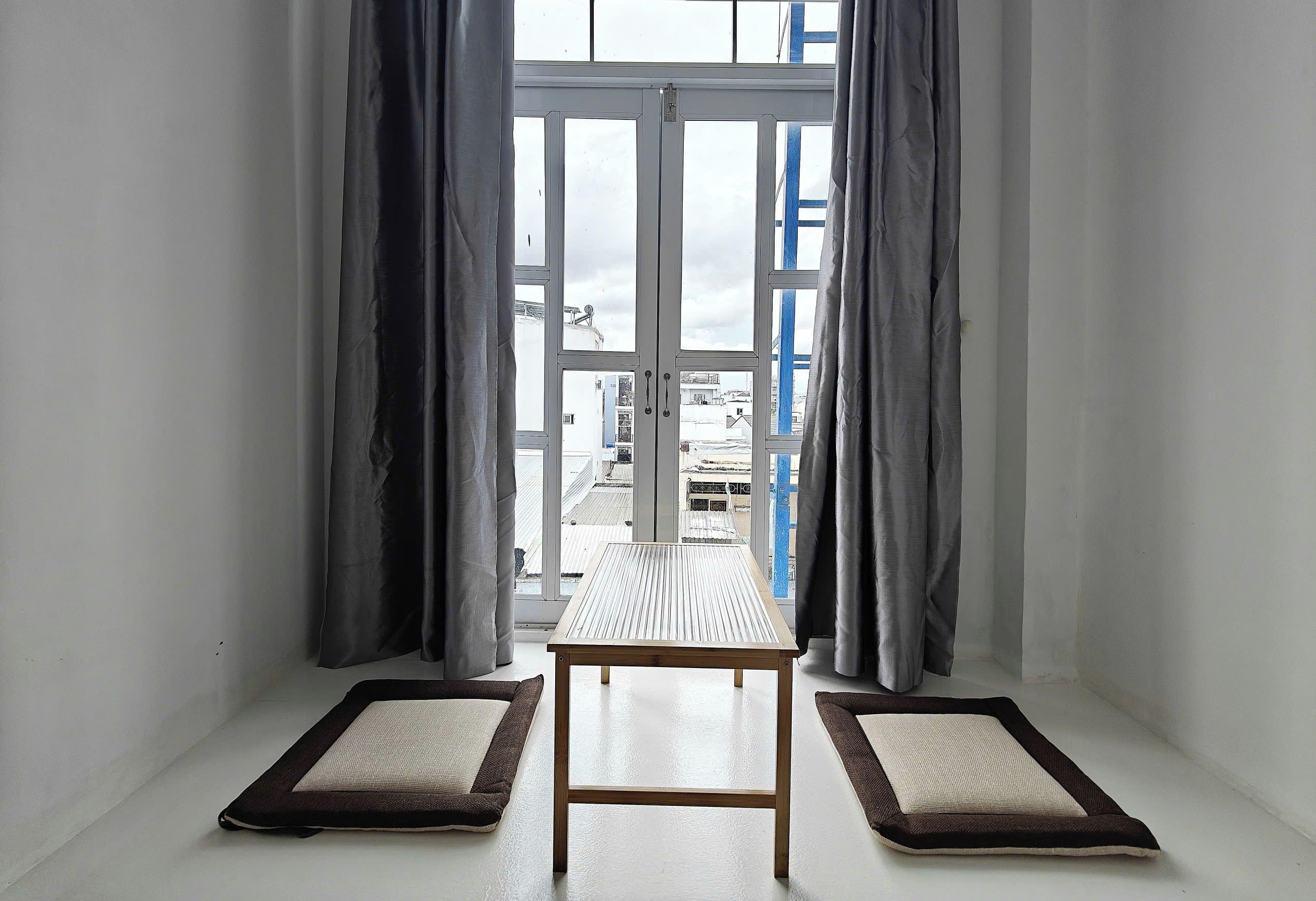 Una habitación con una mesa, dos camas para mascotas, una ventana con cortinas y vistas a edificios.