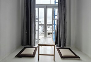 A room with a table and two pet beds, a window with curtains, and a view of buildings outside. - J Guesthouse (Ninh Kieu)