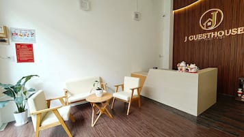 A reception area with a wooden reception desk, two white sofas, a small round table, and a potted plant.