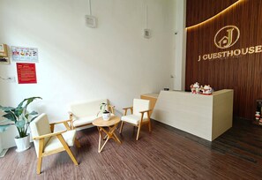 A reception area with a wooden reception desk, two white sofas, a small round table, and a potted plant. - J Guesthouse (Ninh Kieu)