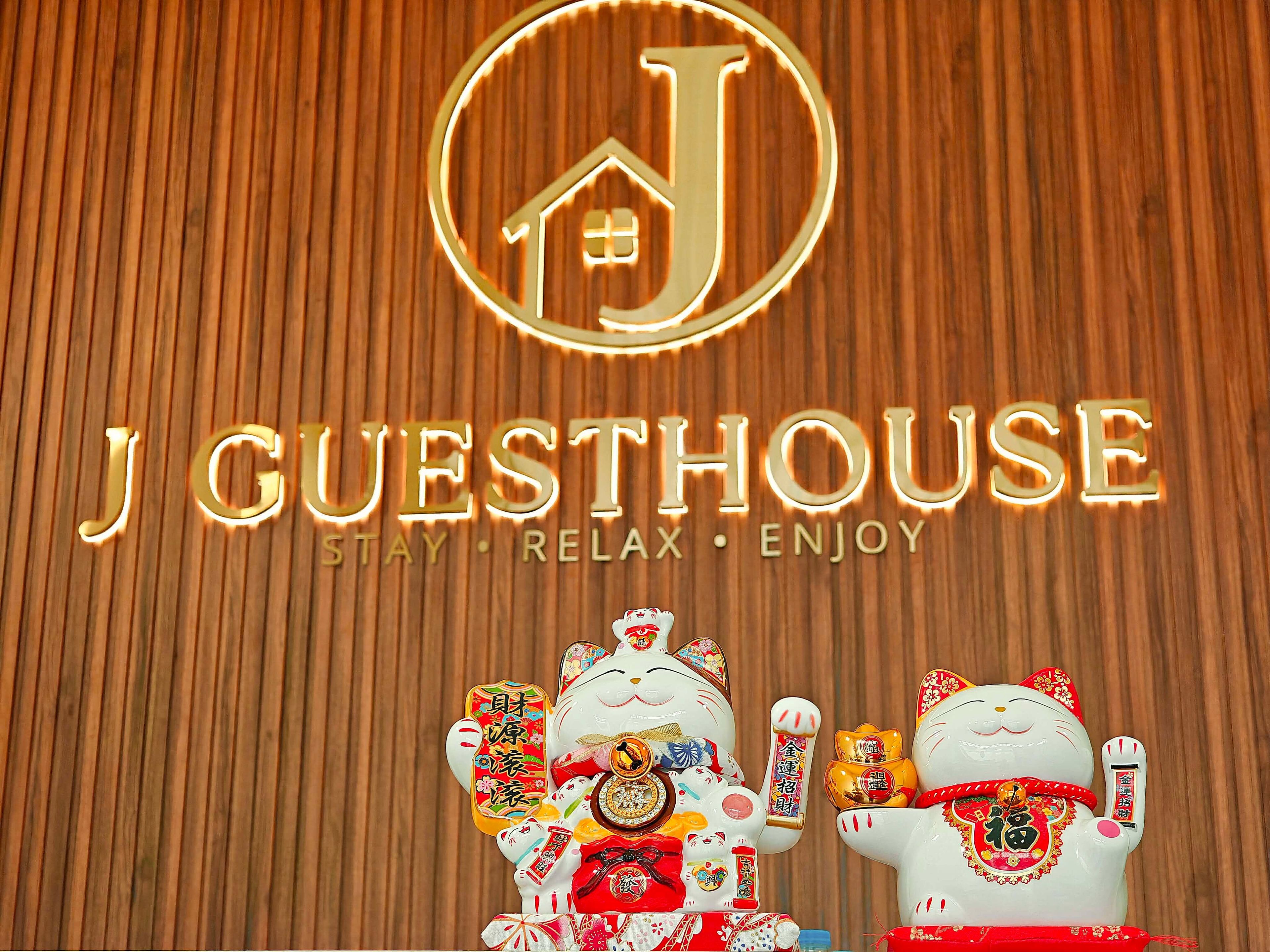 A sign with 'J GUESTHOUSE' and the words 'STAY RELAX ENJOY' against a wooden background.