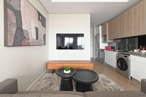 A modern kitchen with a built-in oven, microwave, and dishwasher. There is a dining area with a bench and a small table with a plant. - Sleek Studio with City Skyline Views in Cape Town perfect for your getaway (Cape Town)