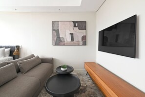 A modern living room with a grey sofa, a round black coffee table, a wooden bench, a wall-mounted TV, and a minimalist abstract painting. - Sleek Studio with City Skyline Views in Cape Town perfect for your getaway (Cape Town)