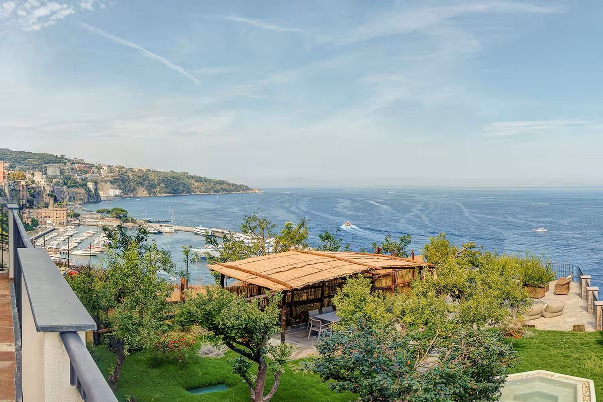A coastal property with a view of the sea, a patio area, and a building with a thatched roof.