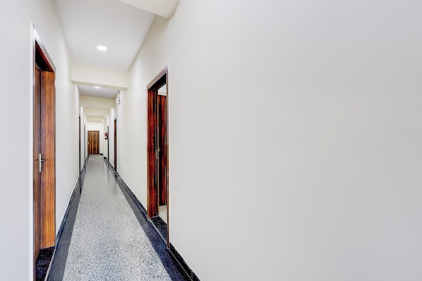 A long, narrow hallway with wooden doors on either side and a carpeted floor. - Collection O Sadar Bazar Gurgaon (Gurugram)