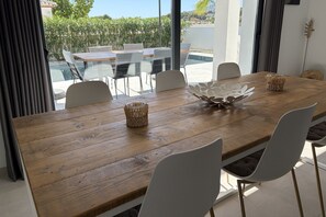 Een eethoek met een houten tafel, witte stoelen en uitzicht op een zwembad en groen.