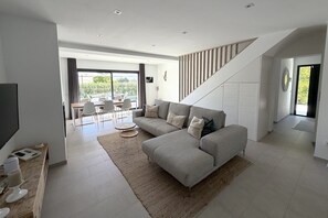 Ein modernes Wohnzimmer mit einem Ecksofa, einem Flachbildfernseher und einem Essbereich mit Tisch und Stühlen.