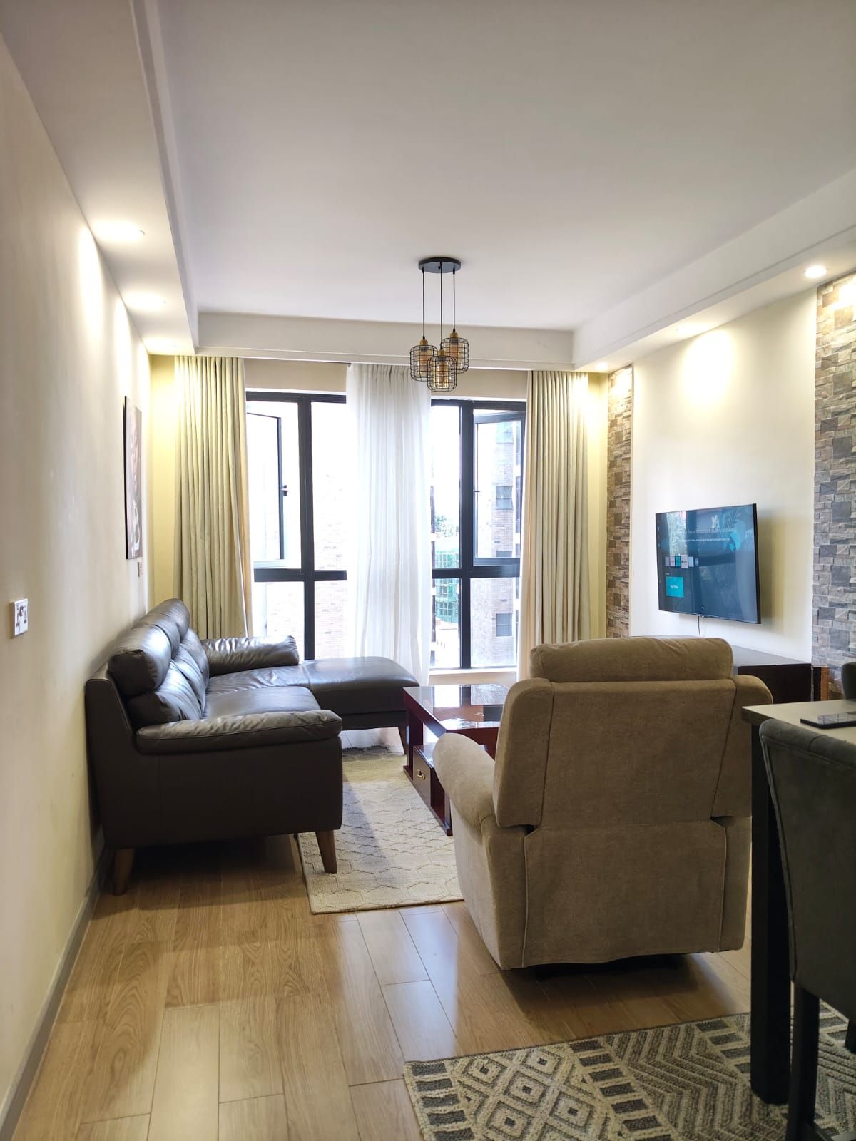 Un salon moderne avec un canapé, un fauteuil et un téléviseur fixé au mur.