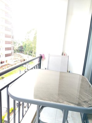 Een balkon met een tafel en stoelen, een whiteboard en uitzicht op gebouwen en groen.