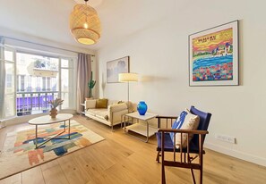 A modern living room with a sofa, a chair, a coffee table, and a floor lamp. There is a large window with a view of buildings outside. - New! N&J - COSY CERVANTES - Central - Spacious (Nice)