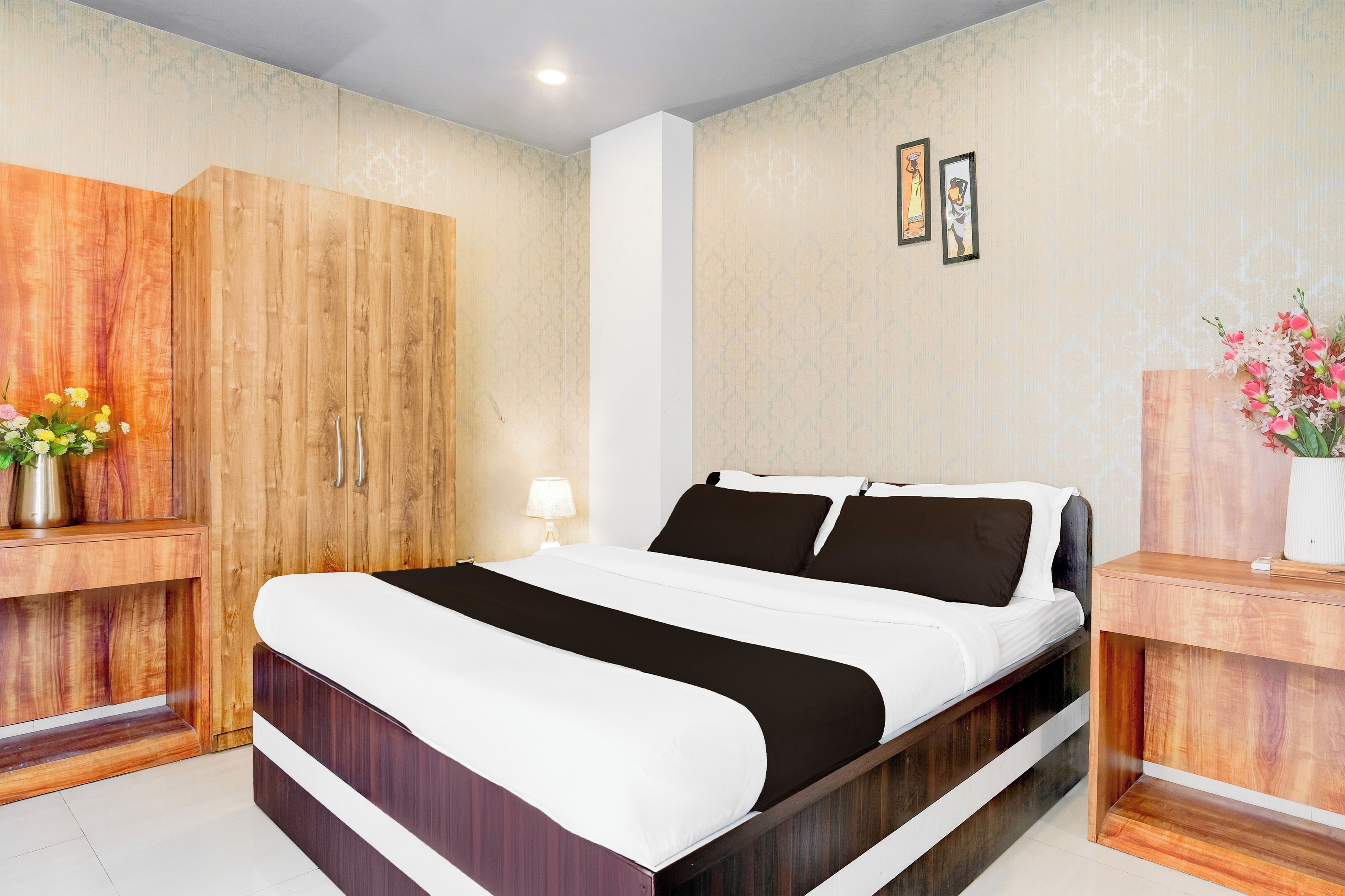 A bedroom with a bed, wooden wardrobe, bedside tables, and a wall with framed pictures.