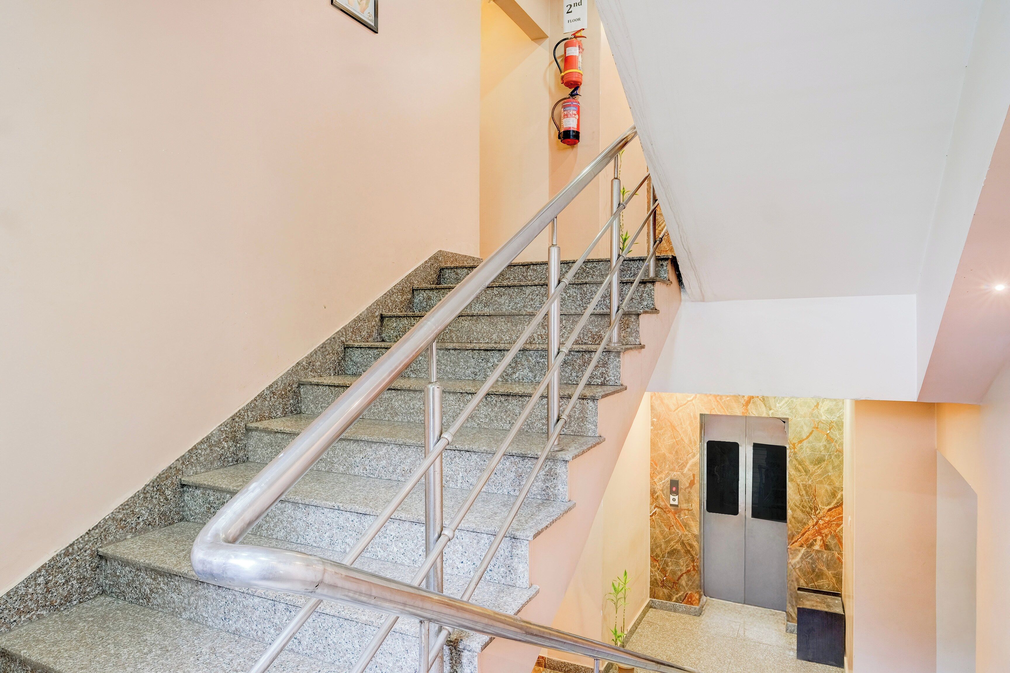 A staircase with metal handrails and granite steps, leading to an elevator area with marble walls.