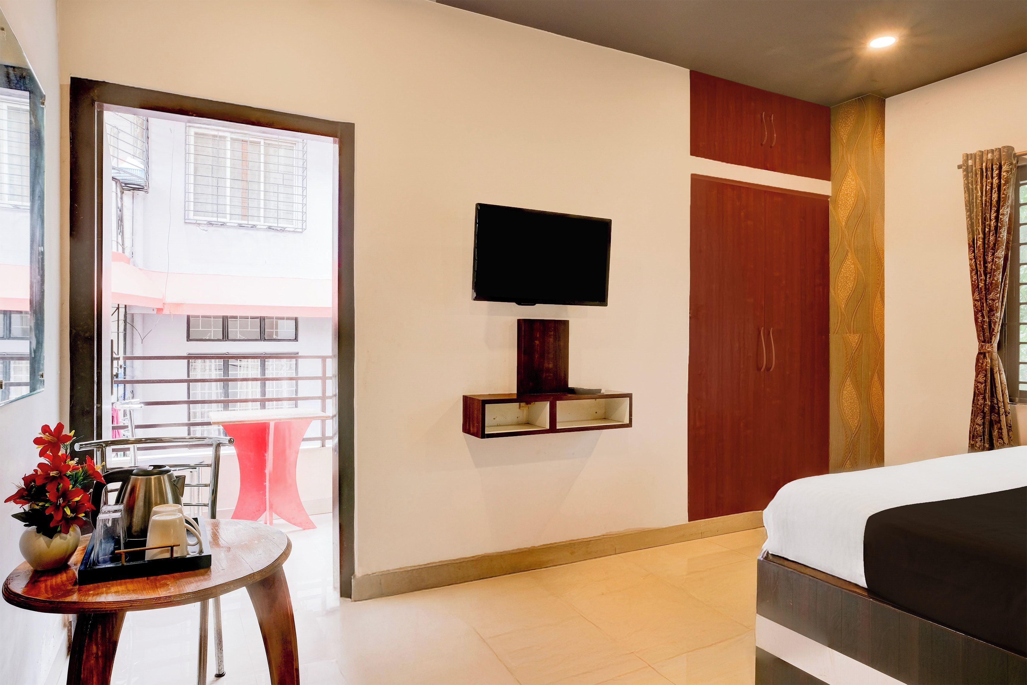 Habitación de hotel con cama, televisor montado en la pared, una mesita con un florero y vistas al exterior a través de una ventana.