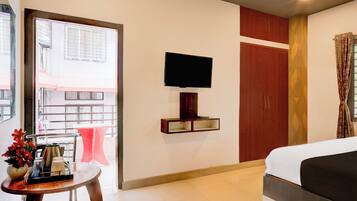 Habitación de hotel con cama, televisor montado en la pared, una mesita con un florero y vistas al exterior a través de una ventana.