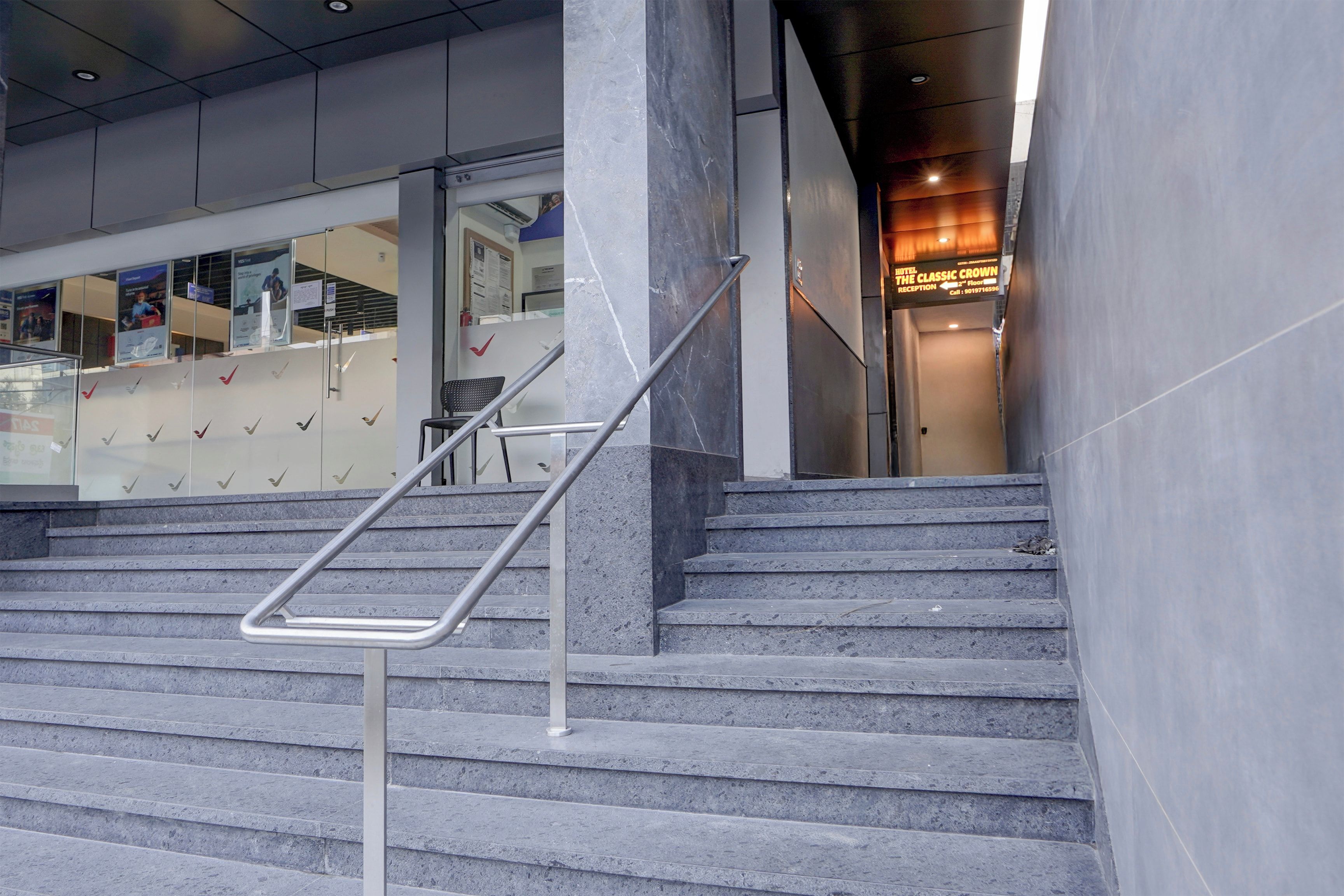 Una escalera con barandillas de metal que lleva a una zona de recepción con un cartel del hotel 'The Classic Crown'.