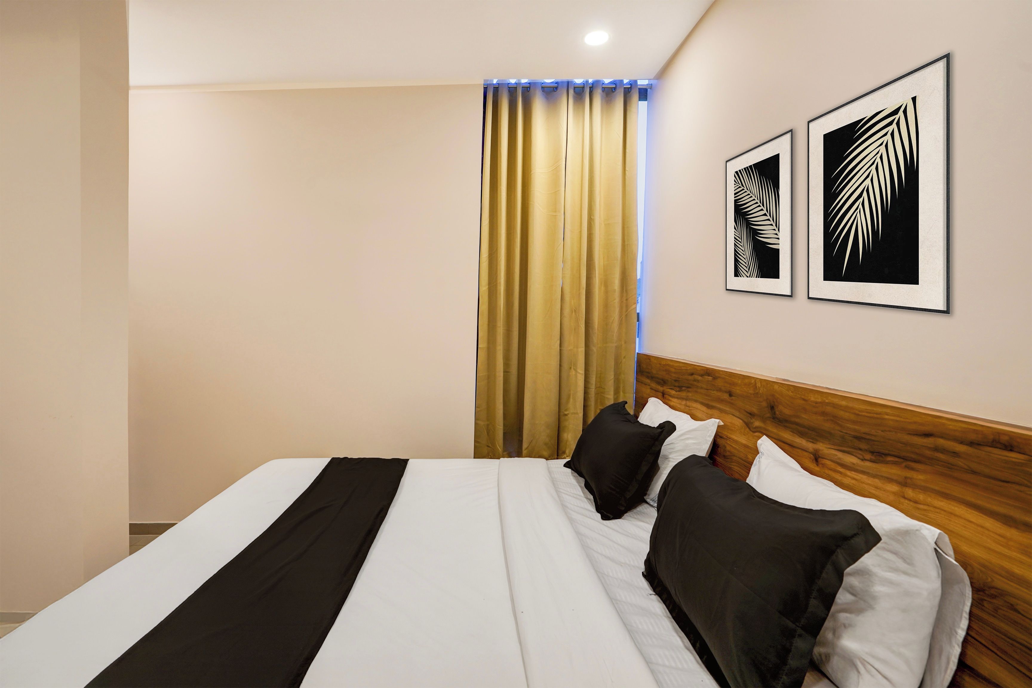 Una habitación de hotel con cama, cabecera de madera y dos diseños de hojas enmarcadas en la pared.