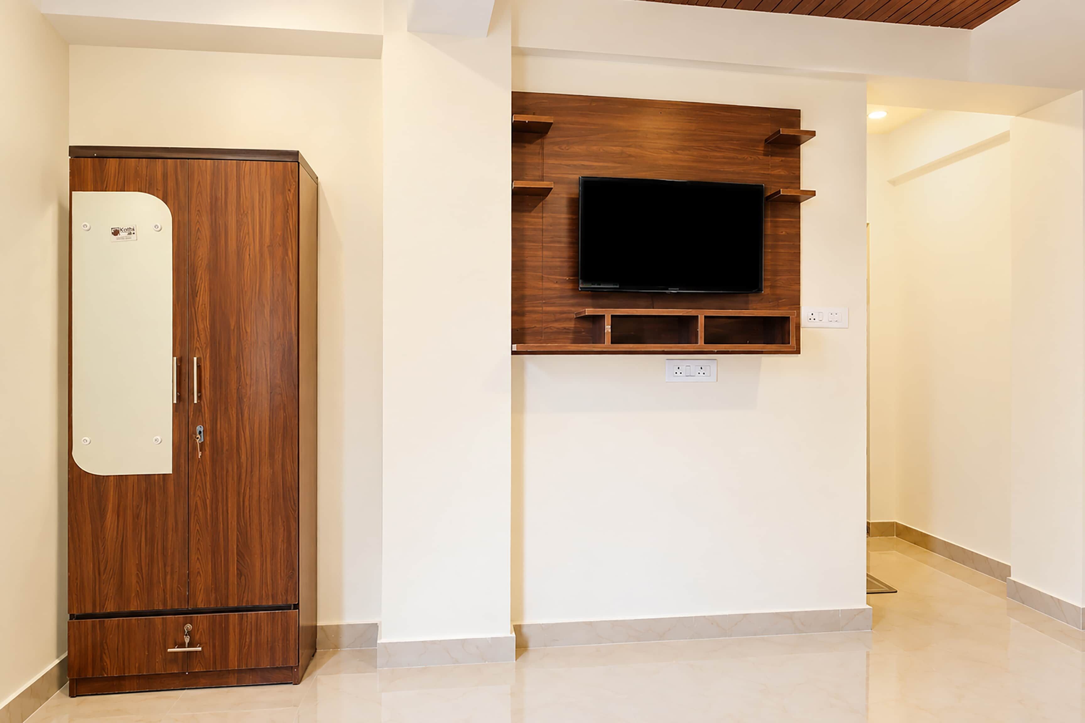 Una habitación con un armario de madera, televisión montada y pared blanca.