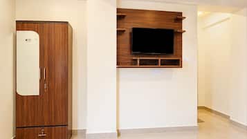 A room with a wooden wardrobe, a mounted television, and a white wall.