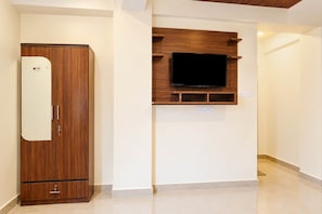A room with a wooden wardrobe, a mounted television, and a white wall.